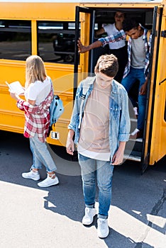 sad teenager schoolboy standing in front of school bus