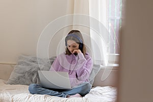 Sad teenager sit on bed using laptop at home