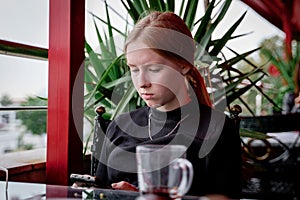 sad teenager sitting on a cafe with bottle water alone. Looking away from camera.