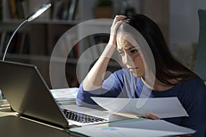 Sad teleworker comparing report on laptop at night at home photo