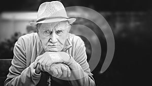 Sad, thoughtful, serious old man in a hat is sitting in an open-air garden. the concept of loneliness and lonely old age. Black