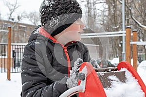 Sad tired boy sitting on a winter snowy children`s playground