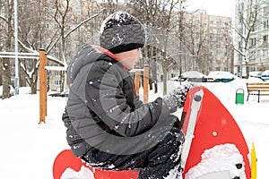 Sad tired boy sitting on a winter snowy children`s playground