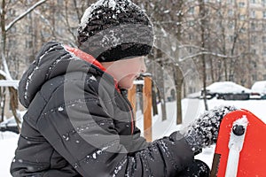 Sad tired boy sitting on a winter snowy children`s playground