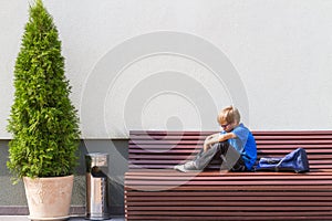 Sad, tired child sitting alone on the bench outdoors.