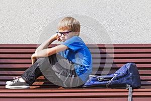 Sad, tired child sitting alone on the bench outdoors.