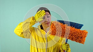 Sad and tired cleaning lady in a yellow suit on a blue background. The concept of professional house cleaning. The