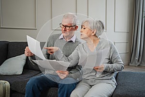 Sad tired disappointed middle aged senior couple sit with paper document. Unhappy older mature man woman reading paper