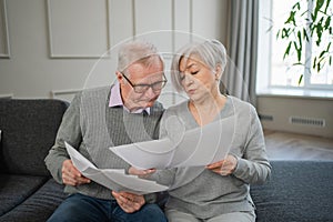 Sad tired disappointed middle aged senior couple sit with paper document. Unhappy older mature man woman reading paper
