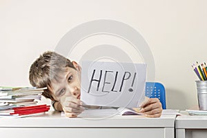 Sad tired frustrated boy sitting at the table with many books and holding paper with word Help. Learning difficulties photo
