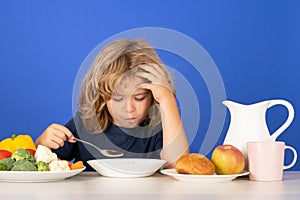 Sad tired kid boy have a dinner. Child eating soup. Young boy with spoon eating soup. Cute healthy hungry child boy