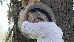 Sad tired woman stands near tree closing eyes, feeling nature energy outdoor