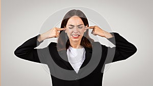 Sad tired young European woman in suit closed ears with hands, closed eyes