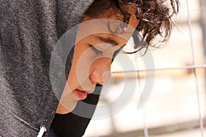 Sad troubled teenager school boy with hood on posing outdoor sitting alone on the street