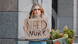 Sad unemployed blonde business woman stands in city looking at camera holds cardboard banner needs work job worried