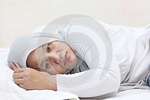 Sad unhappy Asian muslim woman lying on bed with blank stare, hard to sleep thinking of bad situation