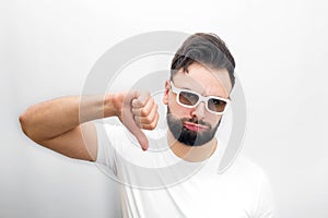 Sad and unhappy bearded young man stand and hold his big thumb down. He dislikes movie. Guy keeps cheeks blowed