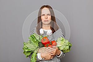 Sad unhappy Caucasian woman holding organic vegetables standing isolated over gray background buying food on market unhappy of