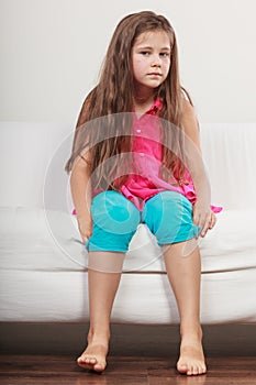 Sad unhappy little girl kid sitting on sofa.