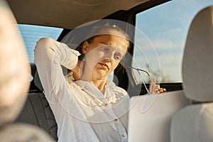Sad unhappy tired woman wearing white shirt in automobile working online on laptop massaging neck feeling exhausted looking at