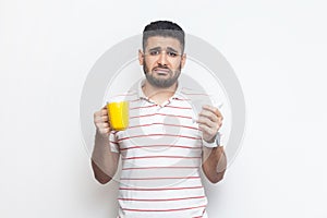 Sad unhappy unhealthy man with yellow cup, looking at camera, feels bad, frowning face