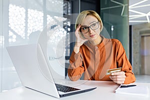 Sad and unhappy woman inside workplace office with laptop holding bank credit card, businesswoman cheated got negative