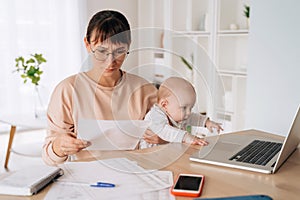 Sad unhappy woman sitting at home office with her little baby