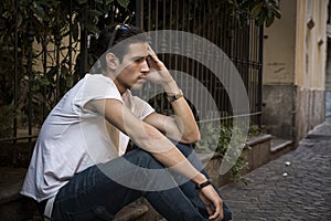 Sad, unhappy young man outdoor, sitting on pavement