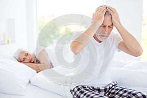 Sad unhealthy gray hair man in checkered pants nightwear sits on