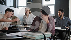 Sad upset abused depressed student sits in classroom at desk alone suffers from bullying aggressive attitude from