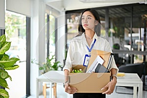 Sad and upset Asian female office worker carrying her belonging, quitting a job, being fired