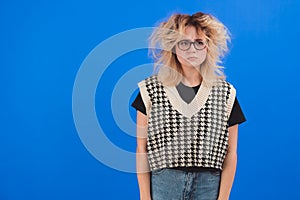 Sad and upset caucasian woman in her 20s with dishevelled hair knitting her brows. Isolated studio shot over blue