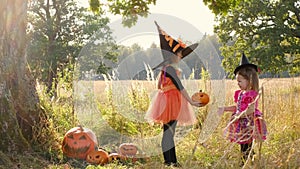 A sad, upset girl in a pink witch dress gives a pumpkin to her sister.