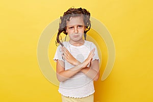 Sad upset little girl with wet hair wearing casual white T-shirt standing isolated over yellow background showing no way gesture