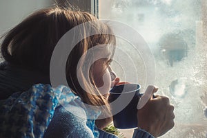 Sad upset lonly beautiful young woman in sweater dreaming near the frozen window