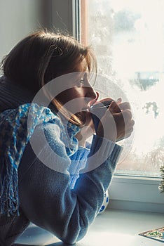 Sad upset lonly beautiful young woman in sweater dreaming near the frozen window