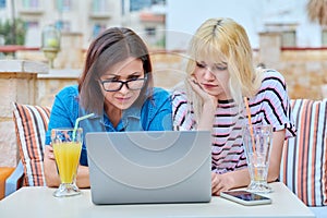 Sad upset serious mom and teenage daughter looking together into a laptop screen.