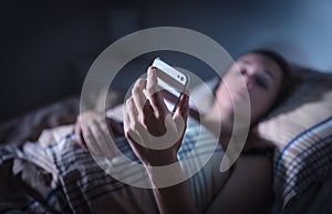 Sad upset woman looking at smartphone at night in bed. Phone call from unknown caller. Sleepless person suffering from stress. photo