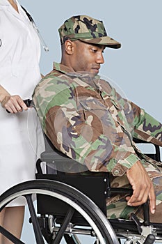 Sad US Marine Corps soldier wearing camouflage uniform in wheelchair assisted by female nurse