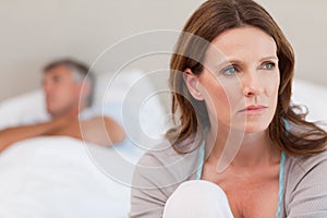 Sad woman on bed with her husband in the background