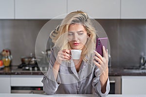 Sad woman chatting on mobile phone on kitchen at home. Depressed woman in the kitchen in the morning. Housewife bad mood