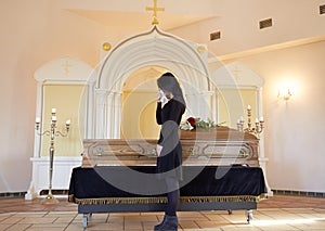 Sad woman with coffin at funeral in church