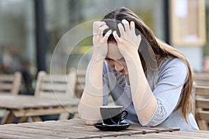 Sad woman complaining alone on a coffee shop terrace