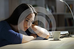 Sad woman complains sitting on a desk at night at home