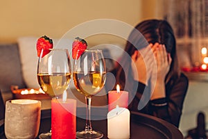 Sad woman crying at home by romantic table setting with wine glasses. Left alone and brokenhearted on Valentine's photo