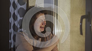Sad woman is depressed sits near window with drops, draws cross on glass.