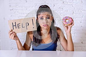 Sad woman on diet holding a sign help resisting temptation to eat chocolate and donuts