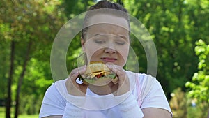 Sad woman eating burger with disgust, lack of willpower, fast food addiction