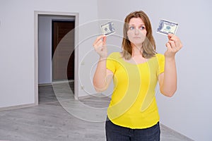 Sad woman in an empty apartment holding torn money. The concept of wasted Finance, credit and problems with dollars