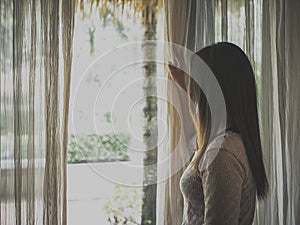 Sad woman holding the curtains open to look out